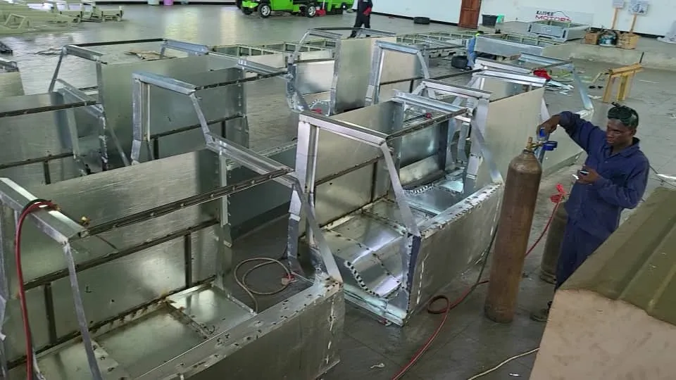 The photo shows ongoing Body in White (BIW) assembly at the Kaypee Motors manufacturing plant, as the vehicle frames move through the welding line.